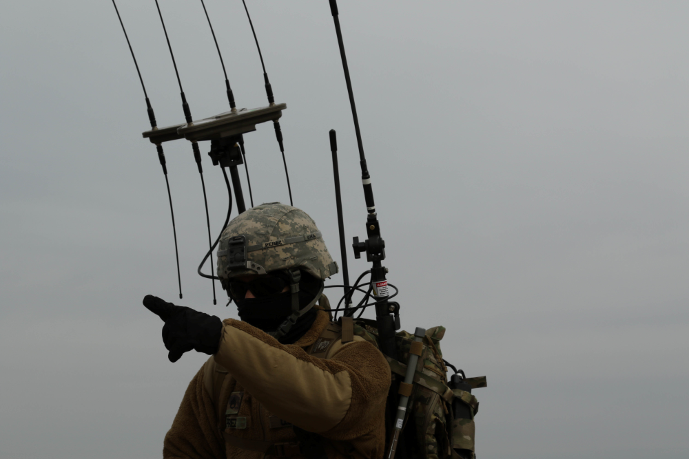 Soldier points while detection equipment is mounted on their back.