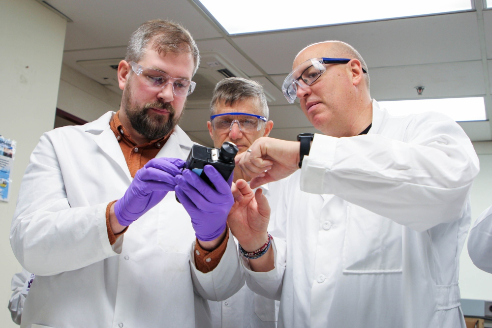 Three scientists inspecting a portable measuring device.