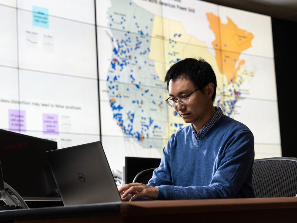 A man looks at the computer monitor with a map in the background