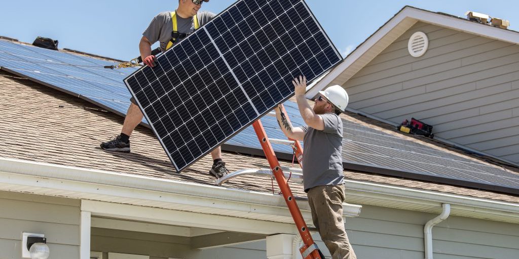Wyatt Whelan, left, and Eric Roberts, both PosiGen install supervisors, move a photovoltaic (PV) panel to a roof on May 11, 2018, in the Dover Family Housing community at Dover Air Force Base, Delaware. Depending on the size of the housing unit, installation of the PV panels generally takes three to five days (U.S. Air Force photo by Roland Balik).