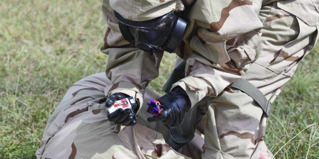While wearing MOPP Level-4 gear, a test player prepares to use a ROCS auto-injector on a simulated casualty (photo credit:  Jose Rodriguez, MEDCoE).