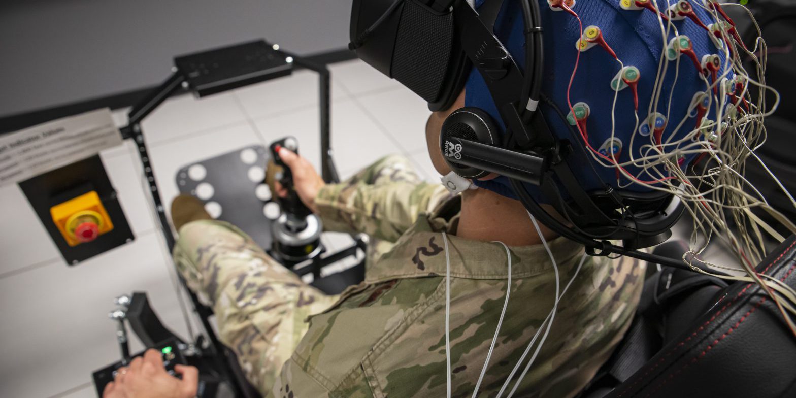 An Air Force Master Sergeant performs an exercise with virtual reality goggles and wires connected to his head.