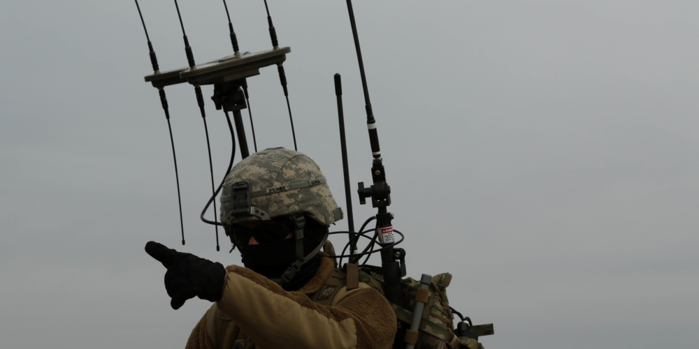 Soldier points while detection equipment is mounted on their back.