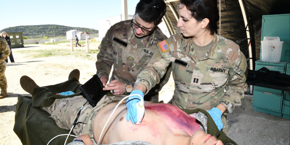 Medical Military Personnel using new ultrasound equipment on other military personnel.