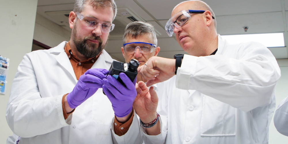 Three scientists inspecting a portable measuring device.