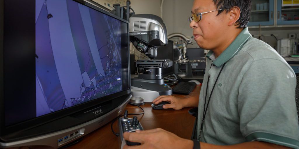 Sandia National Laboratories researcher Guangping Xu employs a digital optical microscope to examine the unusually hard coatings his lab has produced. The aim is better, cheaper protection of instruments and drivers in danger of fast-moving debris flung by Sandia’s Z machine when it fires. The coatings offer many other possibilities as well (photo by Bret Latter).